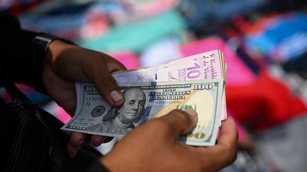 A vendor counts Venezuelan bolivar and US dollar banknotes at La Hoyada market in Caracas on December 23, 2025. (Photo by Federico PARRA / AFP via Getty Images)