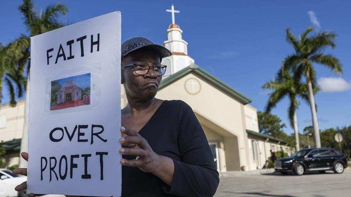 Jennifer Howard sostiene un cartel en protesta por la venta de su iglesia frente a la Iglesia Casa de Dios en Pompano Beach. Miembros de congregaciones del sur de la Florida organizaron la protesta tras enterarse de que iglesias con una larga trayectoria se estaban vendiendo por debajo del valor de mercado, según afirman.