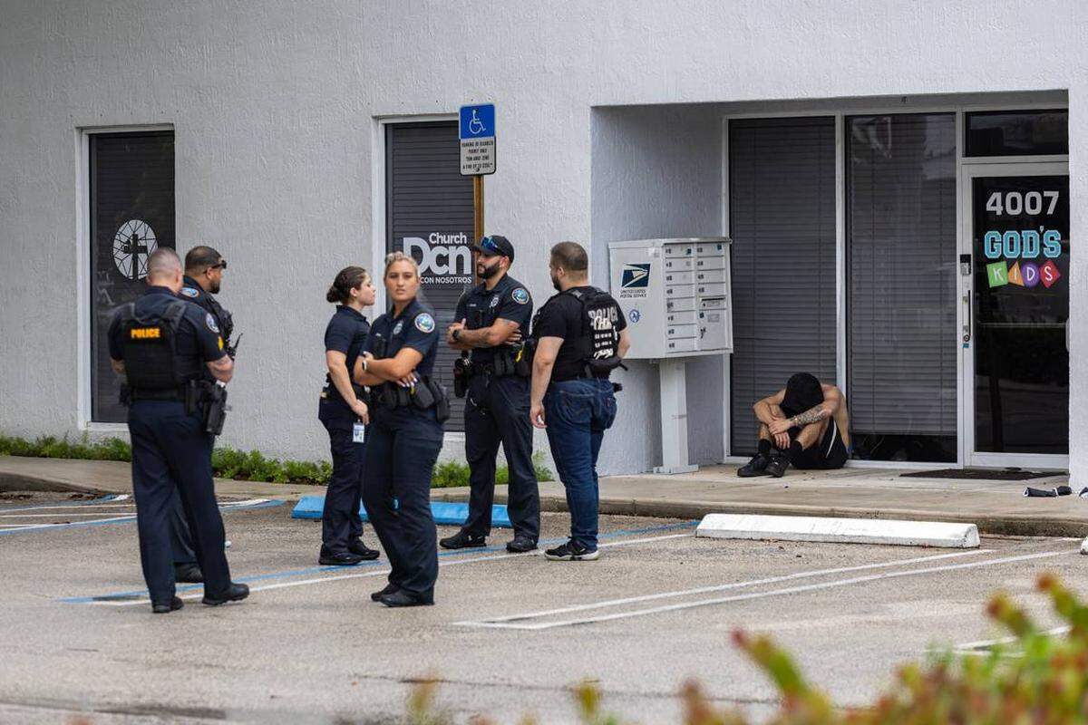 Agentes de policía de la ciudad de Doral junto a un hombre sentado frente a la Iglesia DCN en 4005 NW 79th Avenue después de un tiroteo el viernes 5 de julio de 2024. Una persona murió en el tiroteo y dos personas resultaron heridas, dijo la policía.