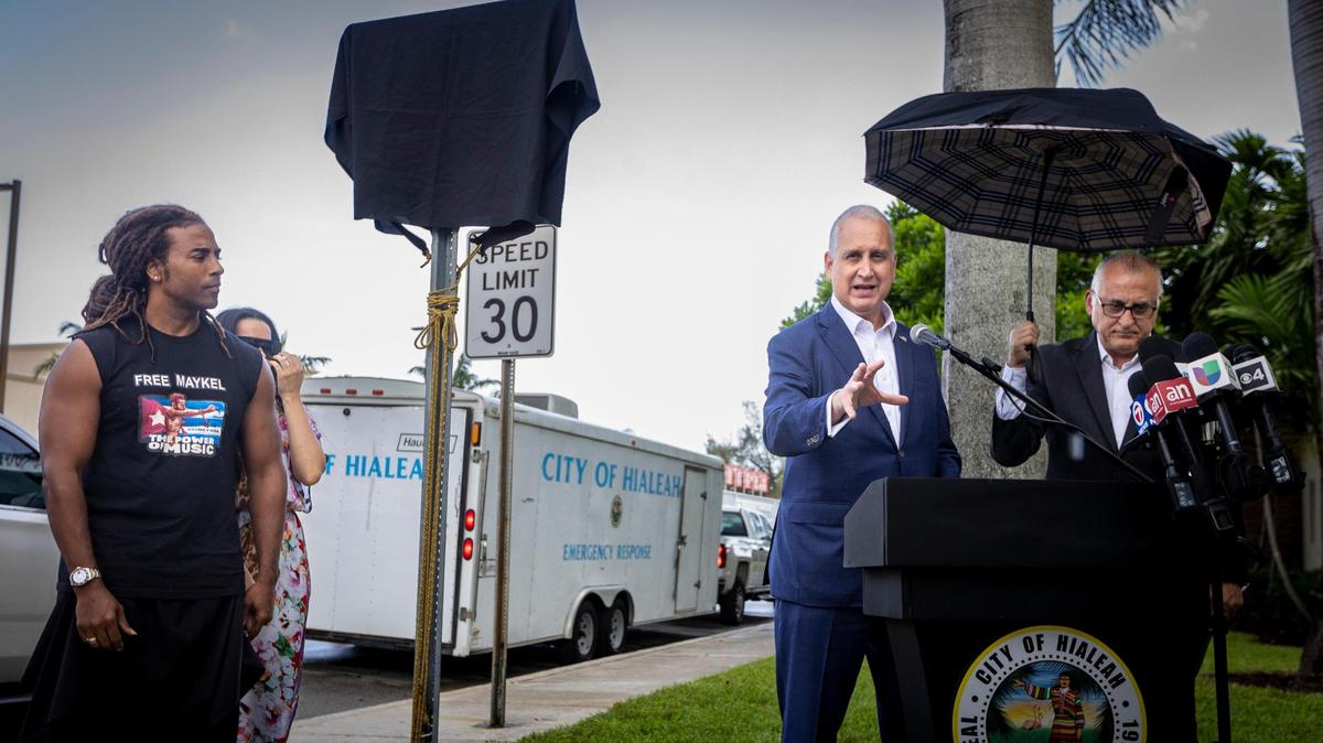 El cantante Yotuel Romero y su esposa Beatriz, a la izquierda, escuchan al congresista Mario Díaz-Balart, centro, mientras habla durante la ceremonia de inauguración de la avenida Patria y Vida, una sección de West 8th Ave en Hialeah, en conmemoración de las protestas de 2021 en Cuba. El evento fue inaugurado por el alcalde Esteban Bovo Jr. HIALEAH, Florida - 10 de julio de 2023 -