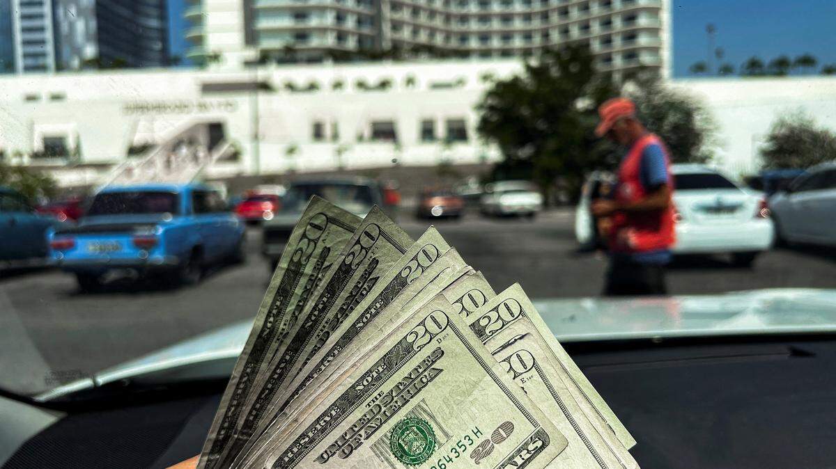 A man holds dollar bills for a picture in front of the new dollar-only supermarket 3ra y 70 in Havana on March 25, 2025. The Cuban government announced that Cubans living abroad can establish businesses in Cuba and invest, but the Cuban legal system offers no guarantees.