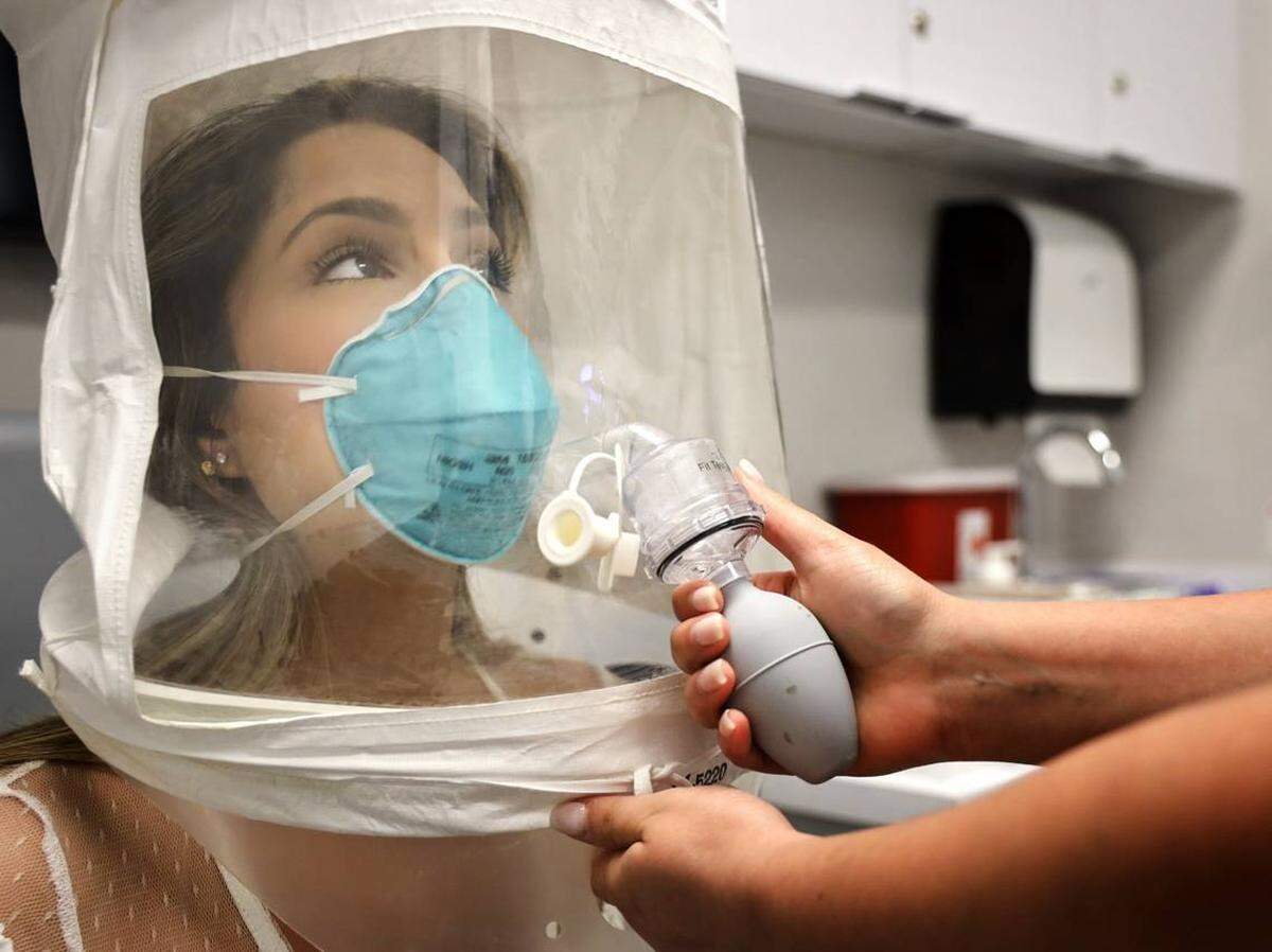La enfermera registrada de la sala de emergencias Erika Juvier, de 24 años, se equipa con un respirador de partículas y una máscara quirúrgica con el uso de una capucha y una solución de prueba de ajuste para asegurarse de que la máscara se ajuste correctamente durante una prueba en la sede de empleados del Nicklaus Children’s Hospital en Miami el 5 de marzo. 2020.