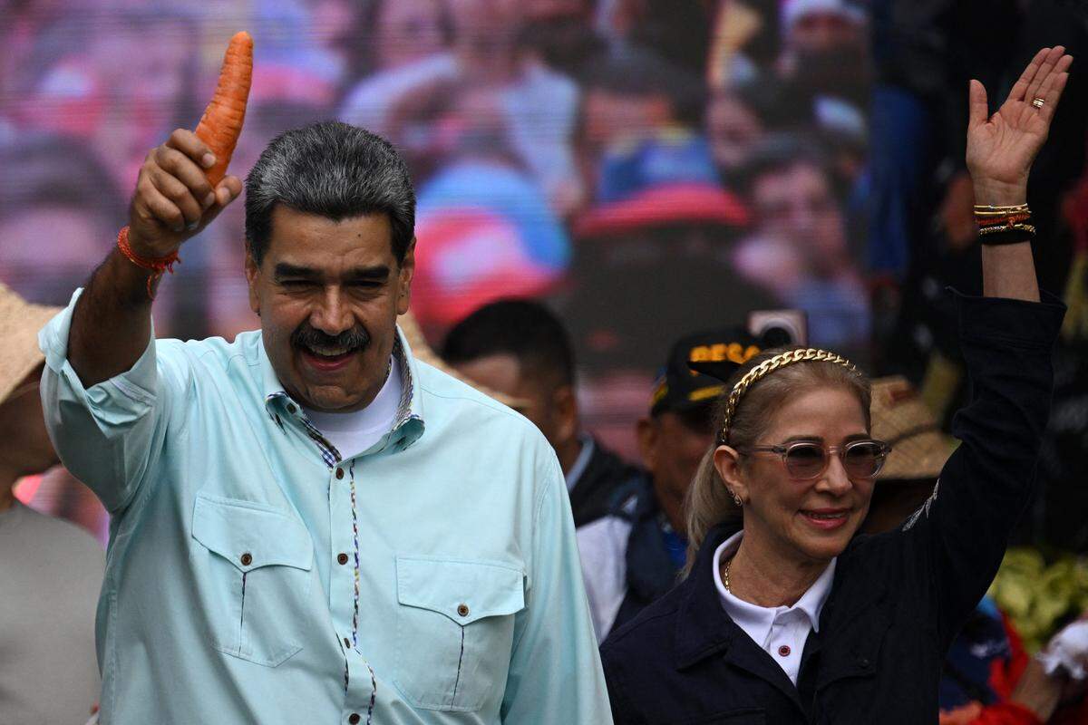 Venezuela's President Nicolas Maduro holds a carrot as he arrives with First Lady Cilia Flores at a rally marking the anniversary of the Battle of Santa Ines, in Caracas on December 10, 2025. (Photo by Federico PARRA / AFP via Getty Images)