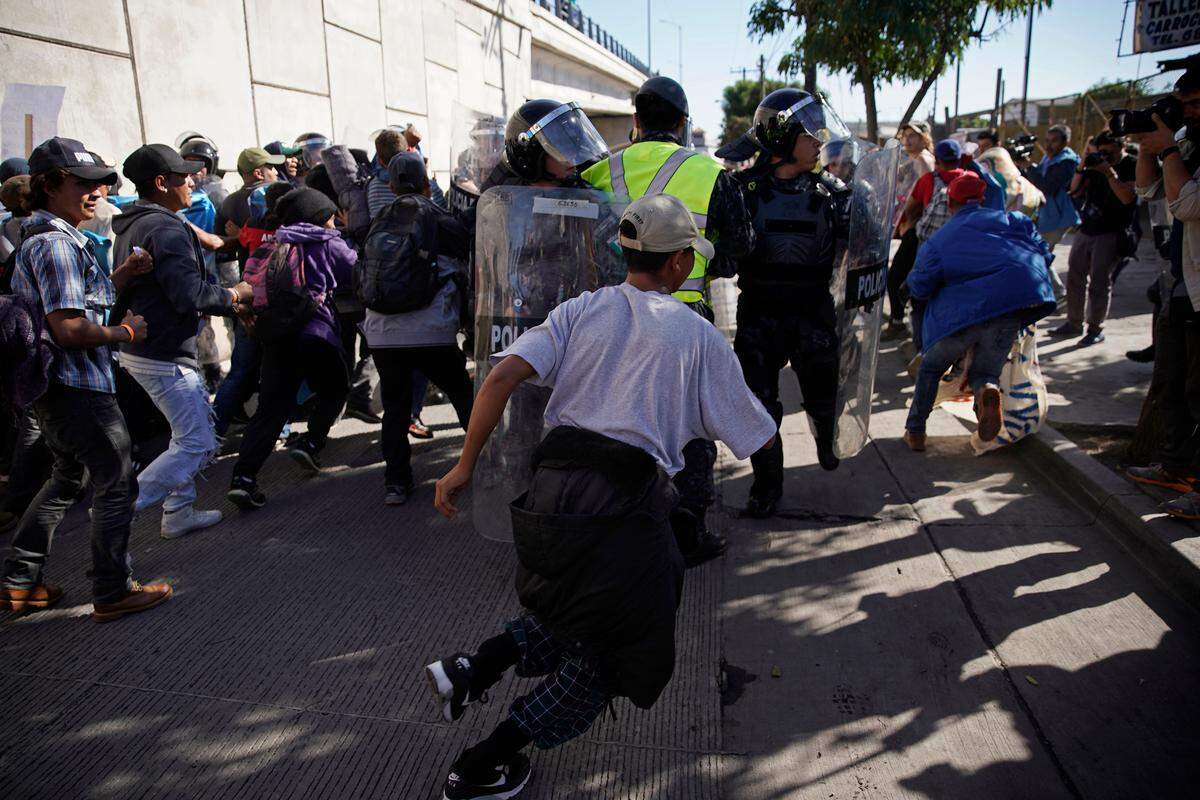 Migrants break past a line of police as they run toward the Chaparral border crossing in Tijuana, Mexico, Sunday, Nov. 25, 2018, near the San Ysidro entry point into the U.S. More than 5,000 migrants are camped in and around a sports complex in Tijuana after making their way through Mexico in recent weeks via caravan.