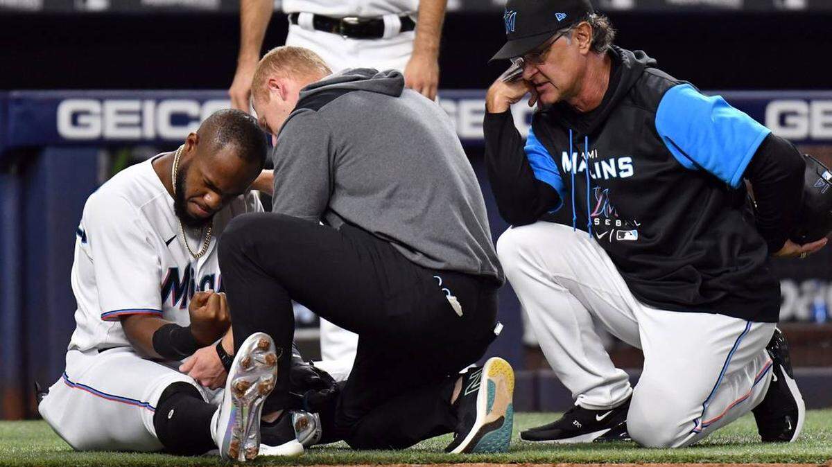 Bryan De La Cruz, de los Marlins de Miami, a la izquierda, es examinado por el personal de entrenamiento mientras el manager de los Marlins, Don Mattingly, a la derecha, observa durante la cuarta entrada de un juego de béisbol, el martes 17 de mayo de 2022