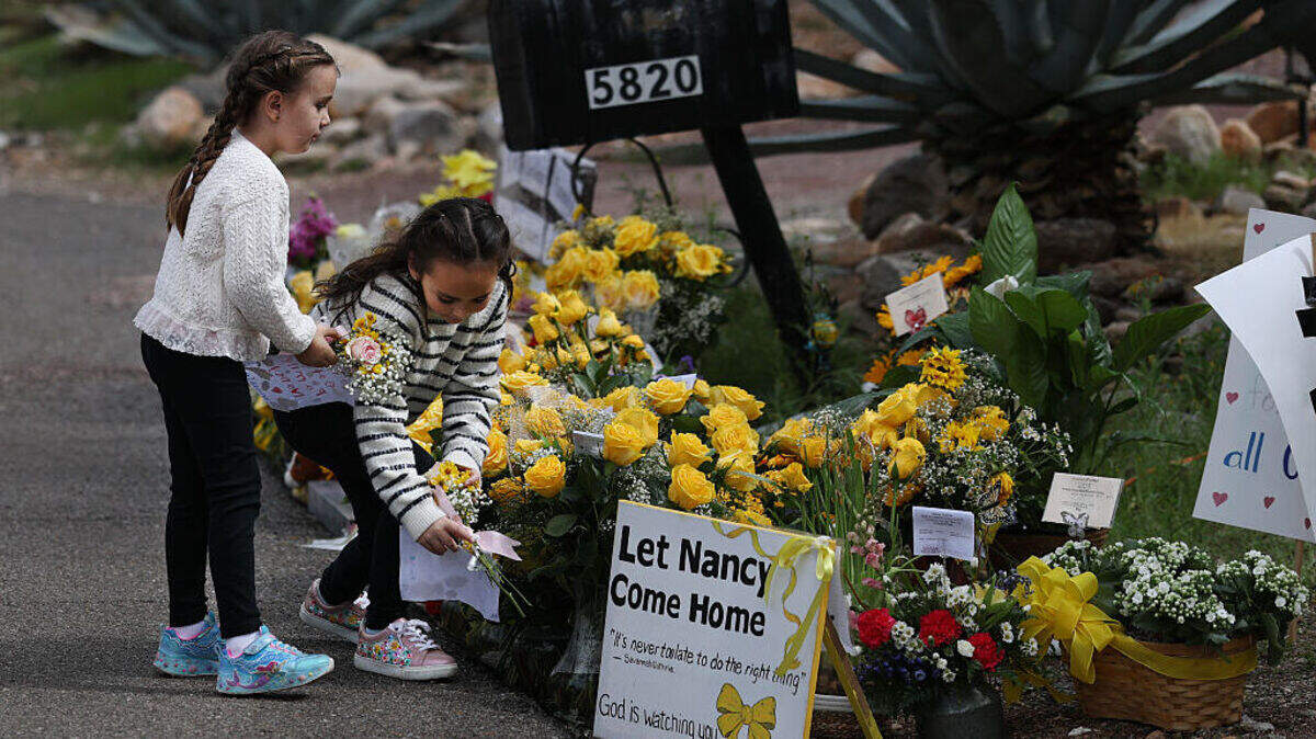 Dos niñas visitan el monumento conmemorativo instalado cerca de la entrada a la residencia de Nancy Guthrie, el jueves 19 de febrero de 2026, en Tucson, Arizona.
