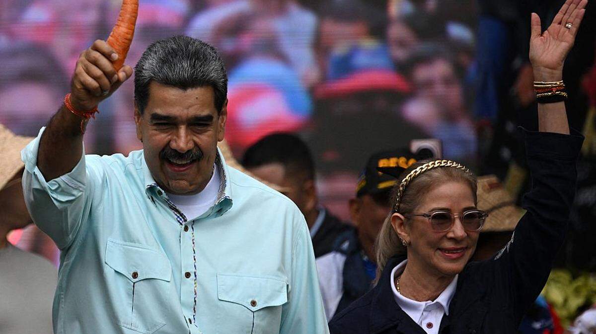 Venezuela's President Nicolas Maduro holds a carrot as he arrives with First Lady Cilia Flores at a rally marking the anniversary of the Battle of Santa Ines, in Caracas on December 10, 2025. (Photo by Federico PARRA / AFP via Getty Images)
