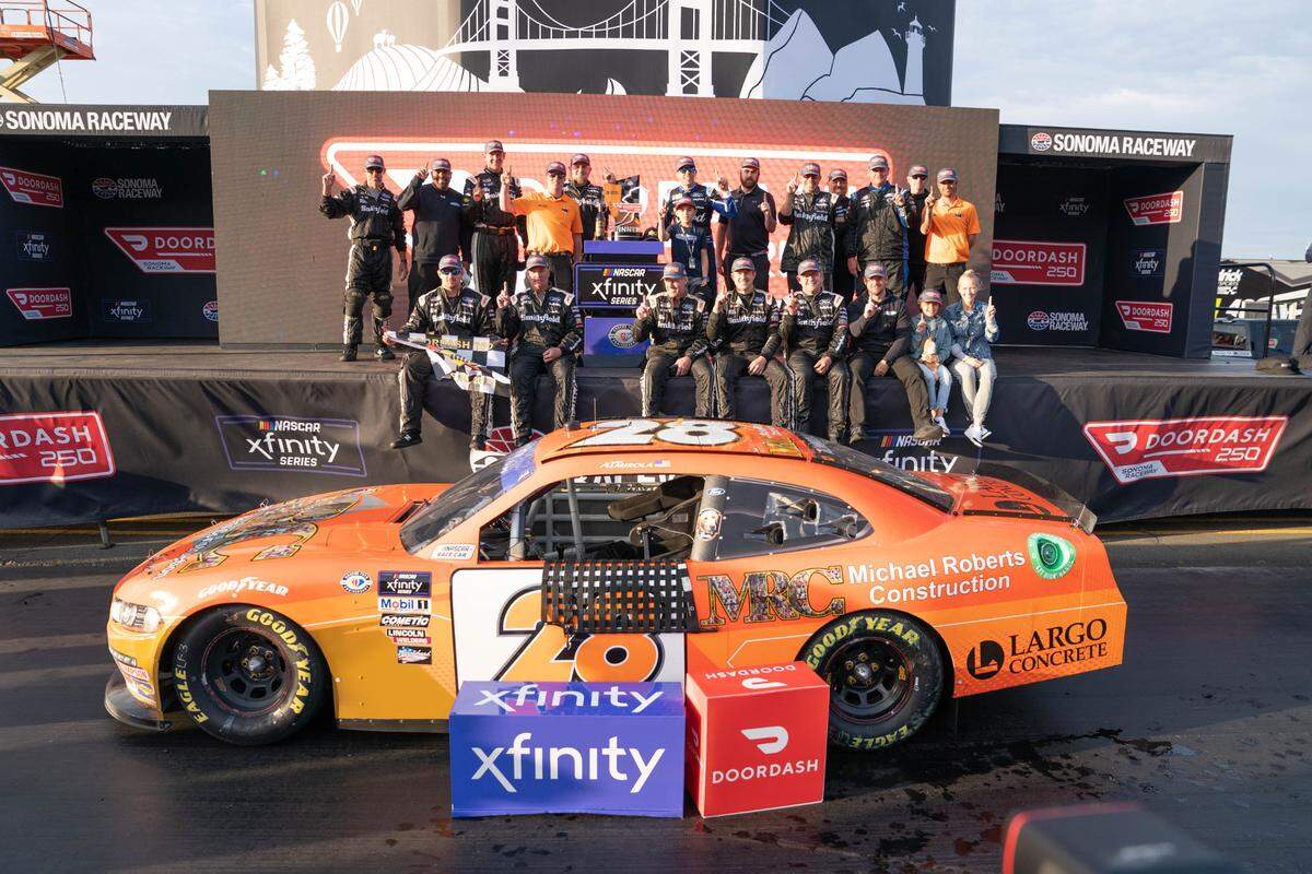 El piloto Aric Almirola celebra con su equipo después de ganar la DoorDash 250 de la Serie Xfinity de NASCAR, en Sonoma, California.
