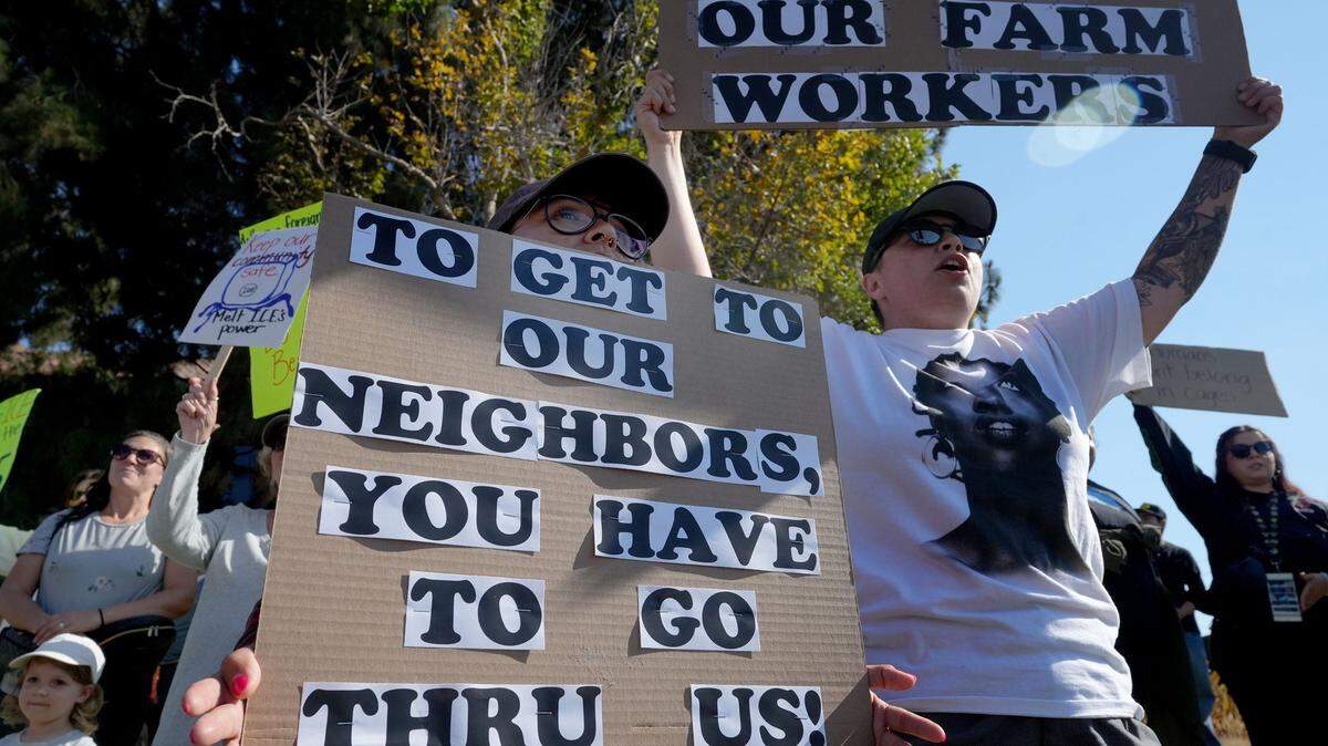 Dos personas muestran carteles durante una protesta contra las redadas de inmigrantes en la granja Glass House Farms, en Camarillo, California, el 14 de julio de 2025. Elcartel de la izquierda dice “Para llegar a nuestros vecinos tendrán que pasar por encima de nosotros”.