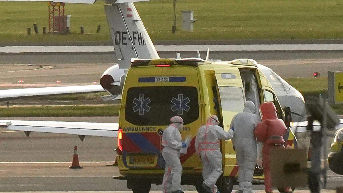 Una persona con un traje de materiales peligrosos (segunda a la der.) es escoltada hacia una ambulancia desde una aeronave médica que, supuestamente, transporta a algunos de los pasajeros del crucero MV Hondius —de quienes se cree que están infectados con hantavirus—, en el aeropuerto de Schiphol, cerca de Ámsterdam, el 6 de mayo de 2026.
