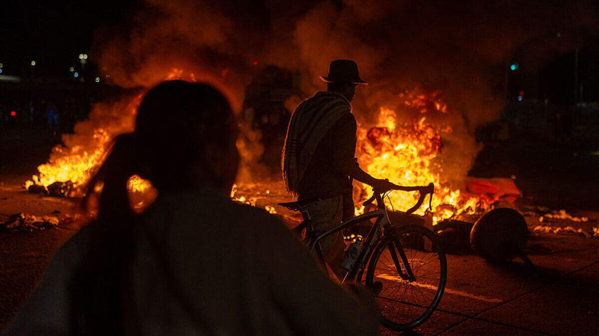 Un hombre camina junto a su bicicleta mientras manifestantes permanecen frente a barricadas en llamas durante enfrentamientos por los resultados preliminares de la segunda vuelta de las elecciones presidenciales en Bogotá, Colombia, el domingo 21 de junio de 2026.