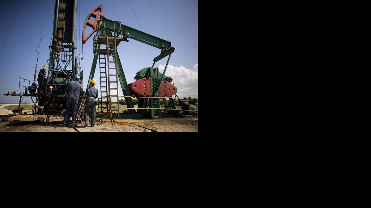 Trabajadores de pie junto a una bomba de pozo de petróleo en Brisas Del Mar, Cuba, Viernes, 30 de enero 2009. AP