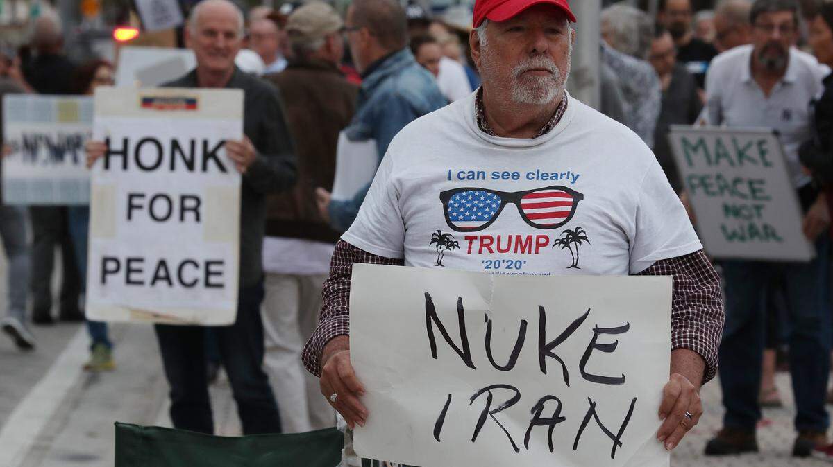 Bob Kunst sostiene una pancarta que dice “Bomba nuclear para Irán” (Nuke Iran), durante una protesta en contra de una posible guerra con ese país del Oriente Medio, el jueves 9 de enero de 2019, en la Antorcha de la Amistad en downtown Miami. Dos pancartas detrás de Kunst dicen “Suena la bocina por la paz” y “Haz la paz, no la guerra”.