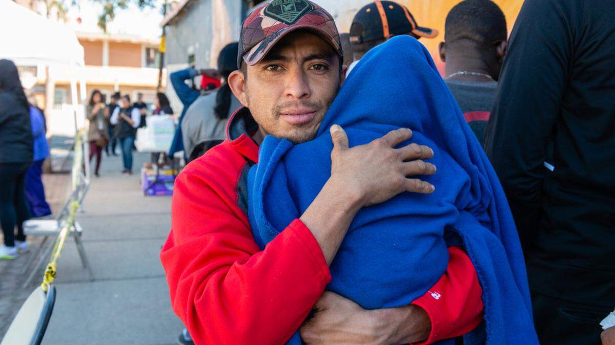 José Manuel Salinas, de Acapulco, Guerrero, sostiene al bebé de su amigo mientras espera en la fila para que lo vea una enfermera. Salinas dijo que le tomó cerca de un mes de caminata y hacer auto stop para llegar a la ciudad fronteriza de Tijuana. Lleva dos semanas luchando contra un resfriado.