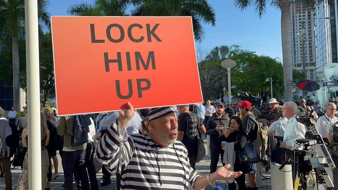 Dominic Santana, de 61 años nacido y criado en Miami está en la corte vestido con un traje de rayas como un prisionero, con una pancarta que dice “enciérrenlo”.