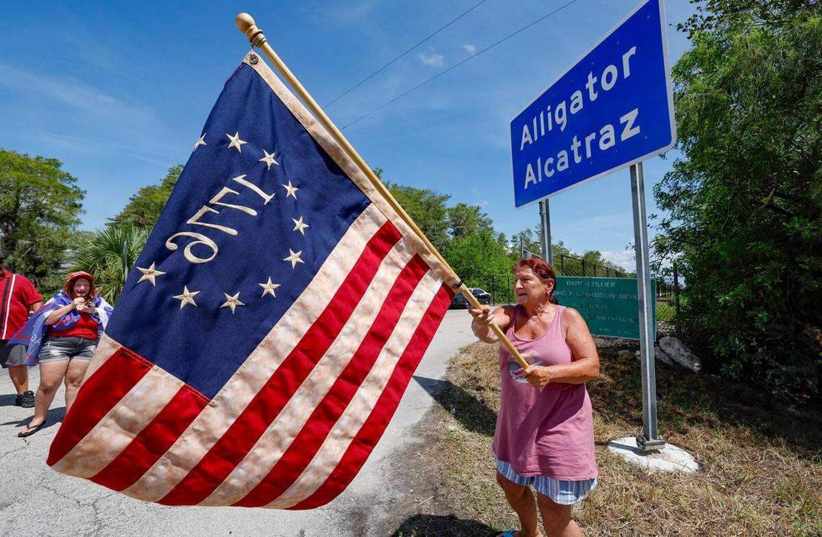 Rena Mourer, quien está a favor del “Alcatraz de los caimanes”, ondea una bandera estadounidense Betsy Ross de 1776 en la entrada principal del centro de detención mientras legisladores de Florida y miembros del Congreso recorren las instalaciones, ubicadas en los Everglades de Florida, a 36 millas al oeste del distrito financiero central de Miami, en el condado de Collier, Florida, el sábado 12 de julio de 2025. FOTO DE AL DIAZ adiaz@miamiherald.com
