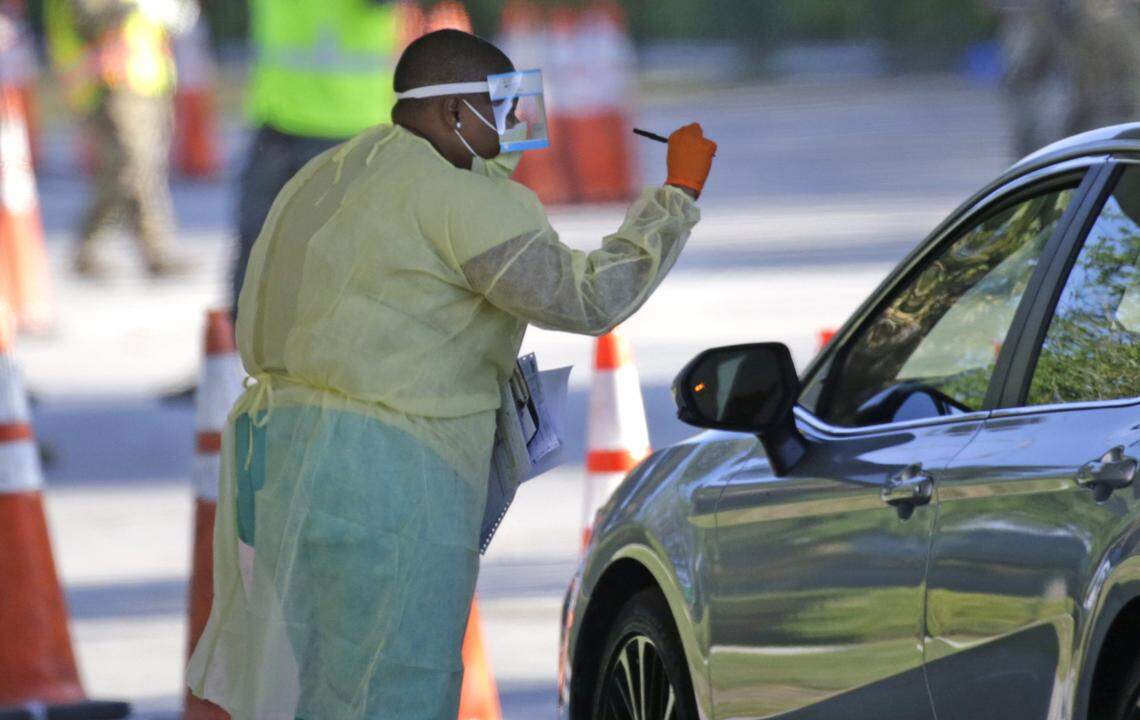 A healthcare worker helps the “check in” process as vehicles line up at the COVID-19 drive-through testing center at Marlins Park in Miami on March 25, 2020, during the coronavirus pandemic.