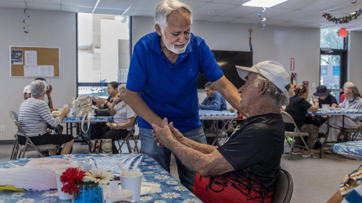 El voluntario y miembro de la organización, Raymundo Ricardo (izq.) saluda a su amigo Rafael Socorro, alias “El Gallegito”, durante la hora del almuerzo en el Centro Familiar Diener JCS en Miami Beach. 