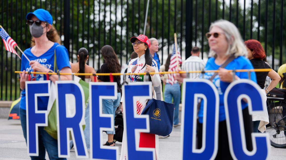 Dos mujeres sostienen una pancarta que dice “Free DC”, “Liberen a DC”, durante una protesta en contra de la orden del presidente Donald Trump de que el gobierno federal controle la policía de Washington D.C., el miércoles 20 de agosto de 2025. En el fondo se ven varios simpatizantes de Trump.