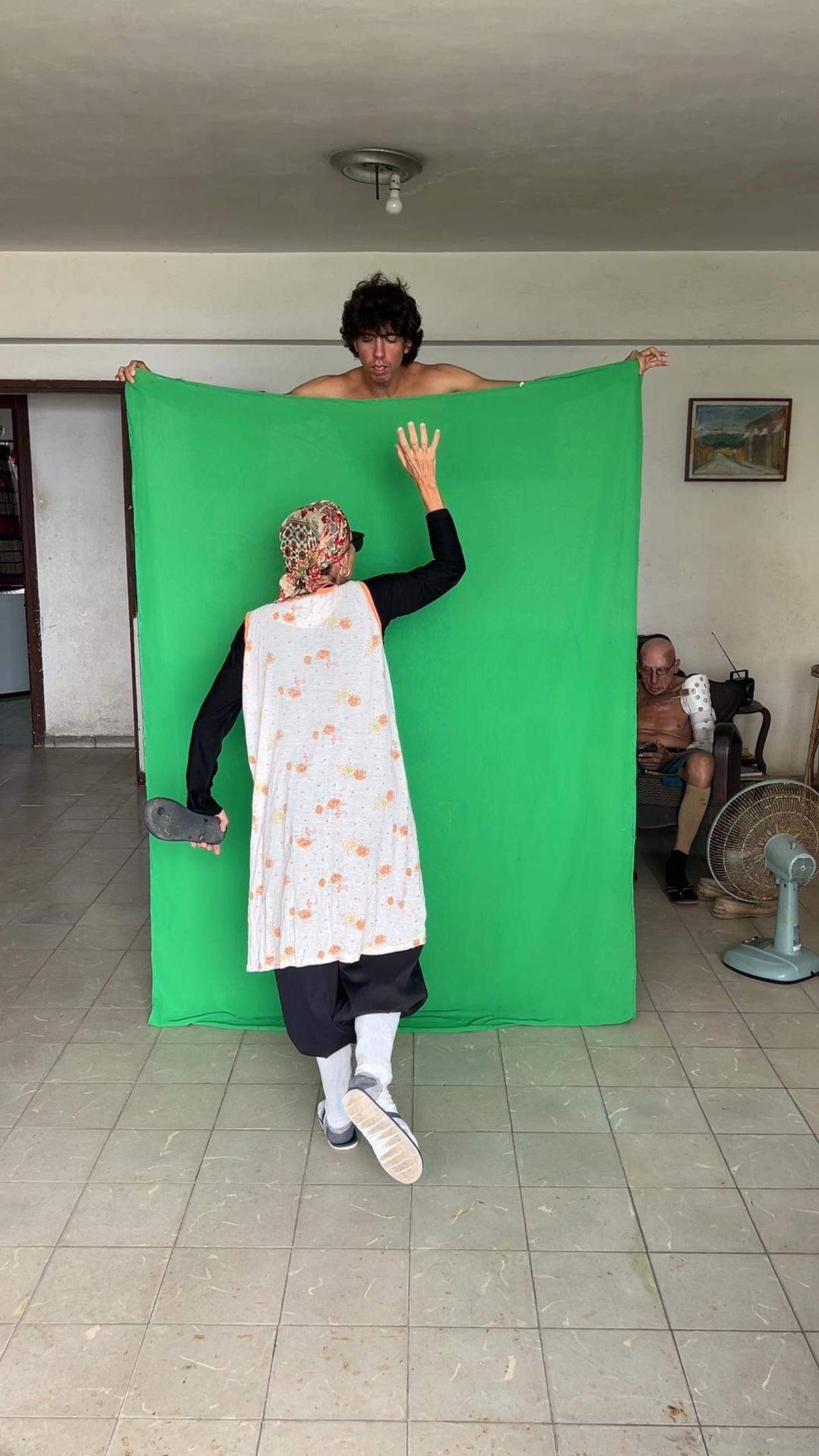Leonardo del Valle Pino holds a green cloth while his mother poses in front of him, holding a flip-flop, before editing the image with special effects for the Tortilla Cubana page on Instagram. 