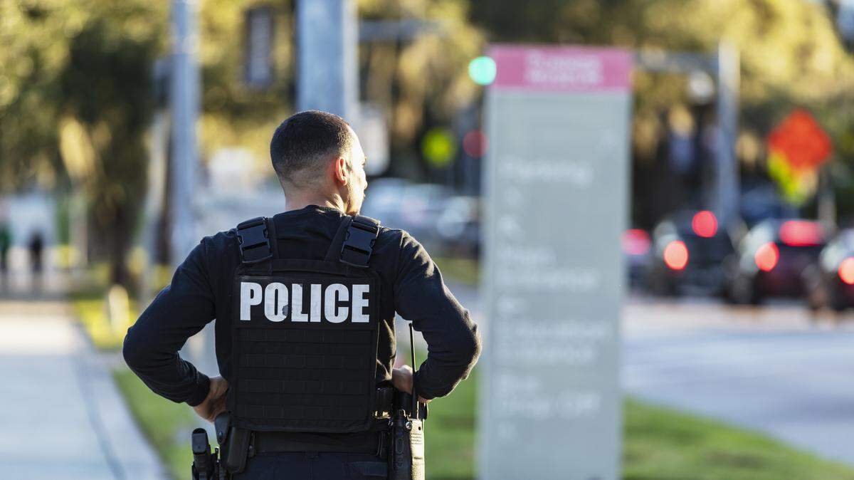 Rear view of an Hispanic police officer patrolling an urban area on foot. He is walking on a sidewalk away from the camera.