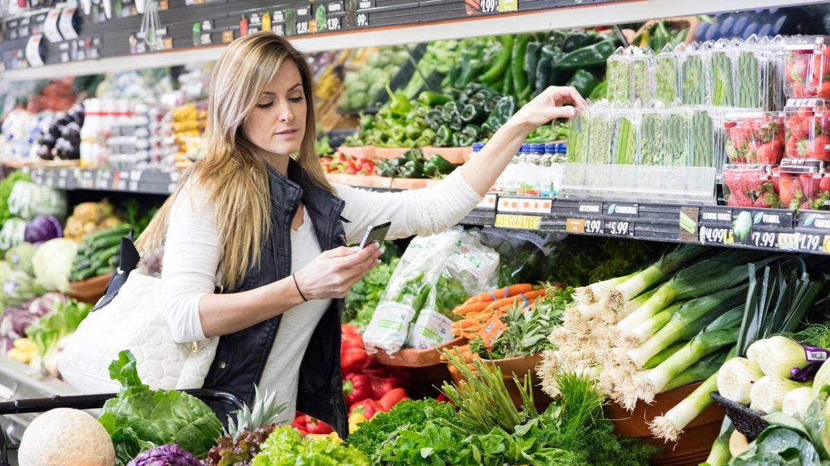 Woman with cart shopping in grocery store in the produce section. Using smart phone