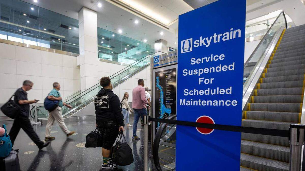 Pasajeros con equipajes le pasan por al lado a una entrada cerrada del Skytrain en el Pasillo D en el Aeropuerto Internacional de Miami (MIA). El servicio se ha cerrado de forma indefinida por daños estructurales.