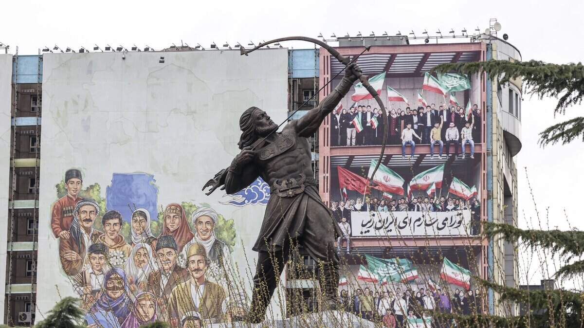 La estatua de Arash el Arquero, uno de los héroes legendarios de Irán, se observa en la plaza Vanak de Teherán, con un enorme cartel publicitario que muestra a personas sobre un mapa de Irán visible al fondo, el 31 de marzo de 2026.