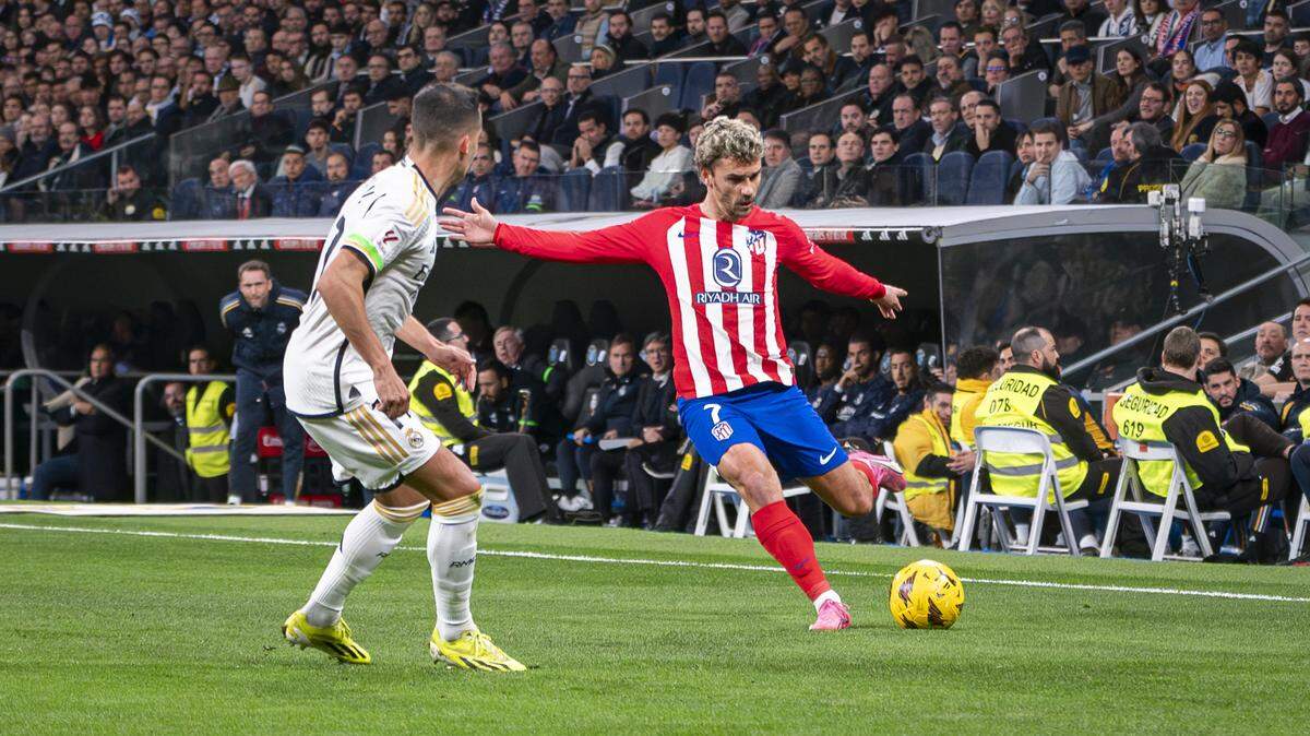 El jugador del Atlético de Madrid Antoine Griezmann (der.) patea la pelota ante el Real Madrid, en el partido de la liga española celebrado el 4 de febrero de 2024 en el estadio Santiago Bernabéu de la capital española.