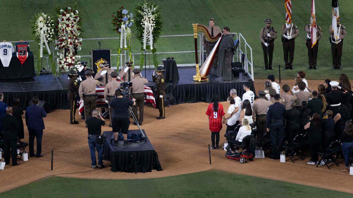 La familia del policía César “Echy” Echaverry, centro, se toma de la mano mientras su ataúd es colocado en el escenario donde se realizó la ceremonia de honor el miércoles 24 de agosto de 2022 en el LodDepot Park en Miami.