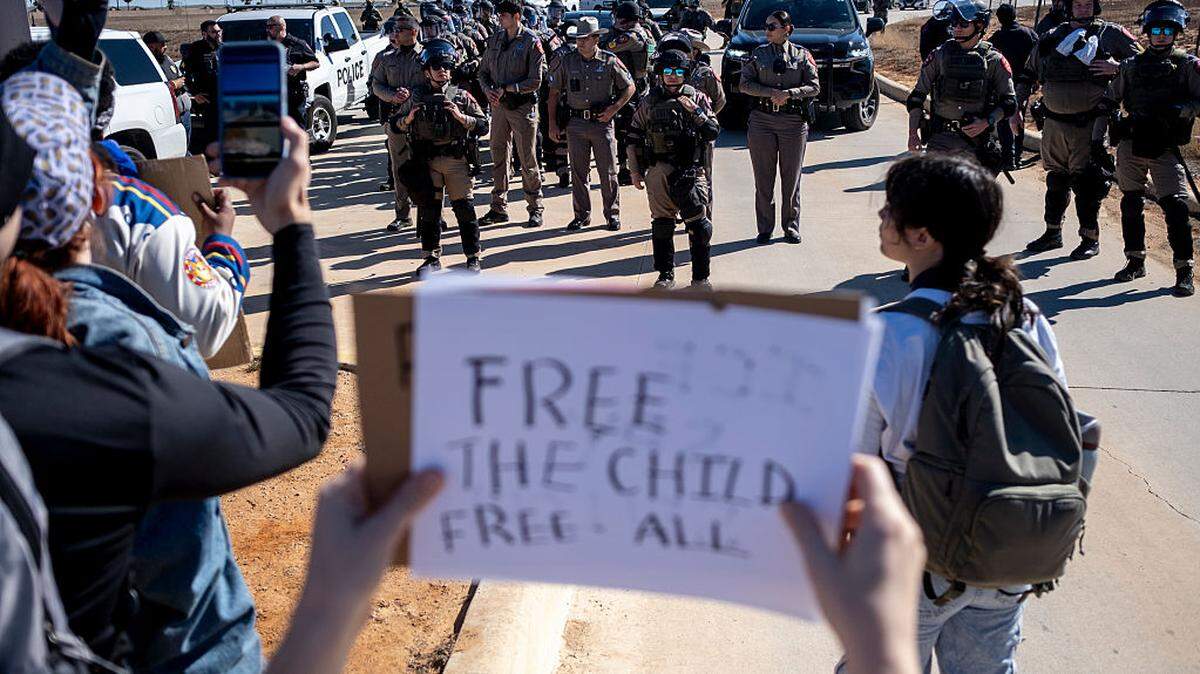 Un manifestante sostiene un cartel que dice “Liberen a los niños, liberen a todos” frente a policías estatales, durante una protesta en contra de la cárcel de inmigrantes de la Policía de Inmigración (ICE) en Dilley, Texas, el miércoles 28 de enero de 2026.