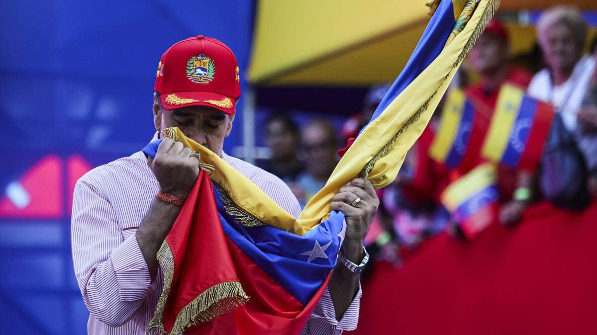 CARACAS, VENEZUELA - DECEMBER 1: President Nicolas Maduro of Venezuela kisses a Venezuelan flag during a protest to support him on December 1, 2025 in Caracas, Venezuela. Supporters gathered at Miraflores to show support and to be part of the swearing-in of the 'Integral Bolivarian Community Commands.' (Photo by Jesus Vargas/Getty Images)