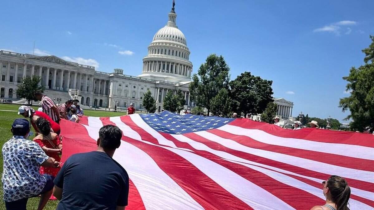 La gente despliega una gran bandera estadounidense cerca del Capitolio de los Estados Unidos como parte de la celebración del Día de la Independencia “Saludo a Estados Unidos” en el National Mall en Washington, DC, el 4 de julio de 2026.