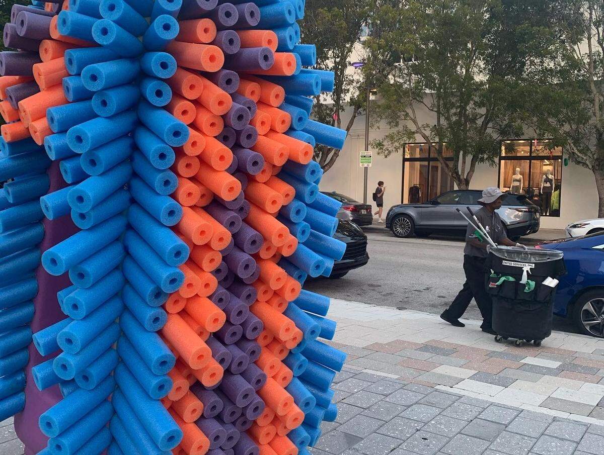 Un trabajador que se ocupa de mantener la limpieza en el Miami Design District pasa junto a una de las esculturas del artista Germane Barnes, que están en numerosos puntos del distrito del diseño en el noreste de Miami durante la semana del arte.