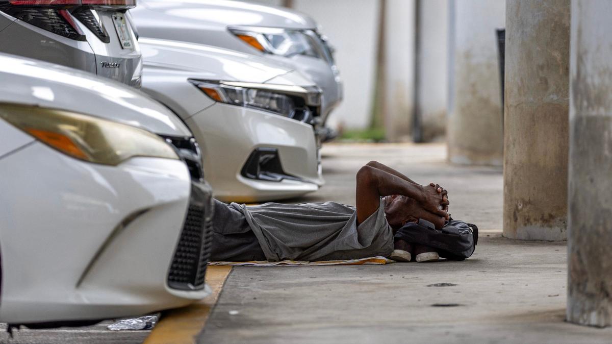 Un hombre duerme en un estacionamiento debajo de la autopista mientras espera que la organización sin fines de lucro ‘One World One Heart’ entregue comidas gratuitas a la población sin hogar el jueves 12 de septiembre de 2024 en Miami, Florida.