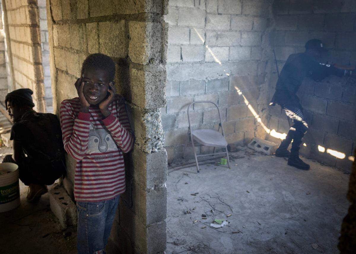 Un niño tapándose los oídos, se queda cerca del hombre a la izquierda que lo estaba ayudando durante un reciente tiroteo de pandillas en Puerto Príncipe. Cientos de miles de niños han sido desplazados por la violencia que azota el país.