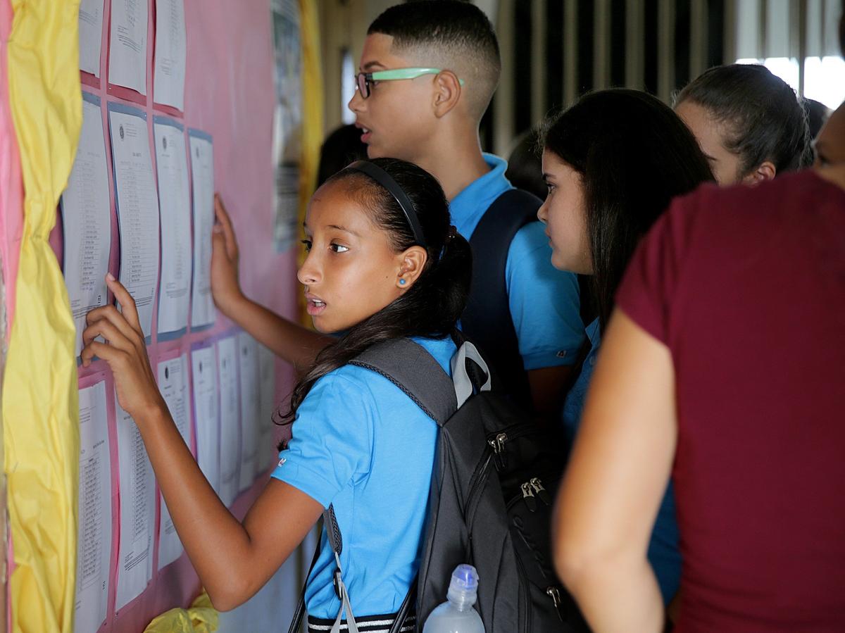 Los alumnos buscan sus nombres y las aulas que le corresponden en las listas colocadas a la entrada de la escuela intermedia pública Rosa Costa Valdivieso, en la localidad puertorriqueña de Yabucoa, el primer día del curso escolar, el lunes 13 de agosto del 2018.