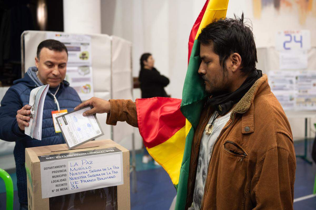 17 de agosto de 2025, Bolivia, La Paz: Un votante sosteniendo la bandera boliviana deposita su voto en una urna durante las elecciones presidenciales de 2025.