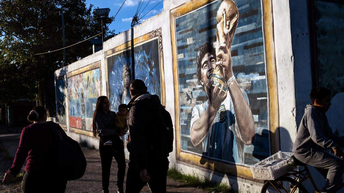 Personas caminan junto a murales que representan al fallecido futbolista diego maradona en su barrio natal de villa fiorito, en la provincia de buenos aires, argentina, el 9 de abril de 2026.