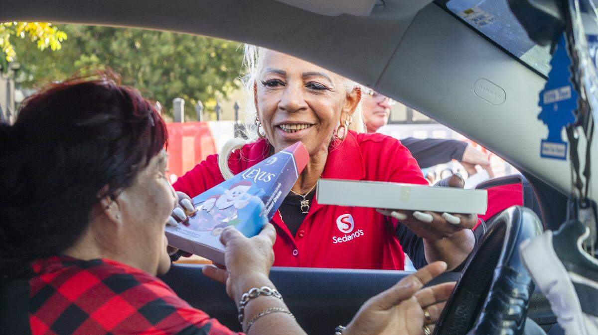 Frida Cárdenas entrega una caja de chocolates a Marina Varona en la distribución de cestas navideñas de la CAMACOL, en diciembre del 2024. En el 2025 la repartición gratis de las cestas con comida es este 10 de diciembre a partir de las 7 a.m., en el LoanDepot Park.