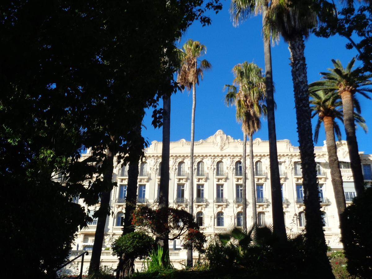 Hotel de la Belle Epoque en Niza precedido por un parque de palmeras.