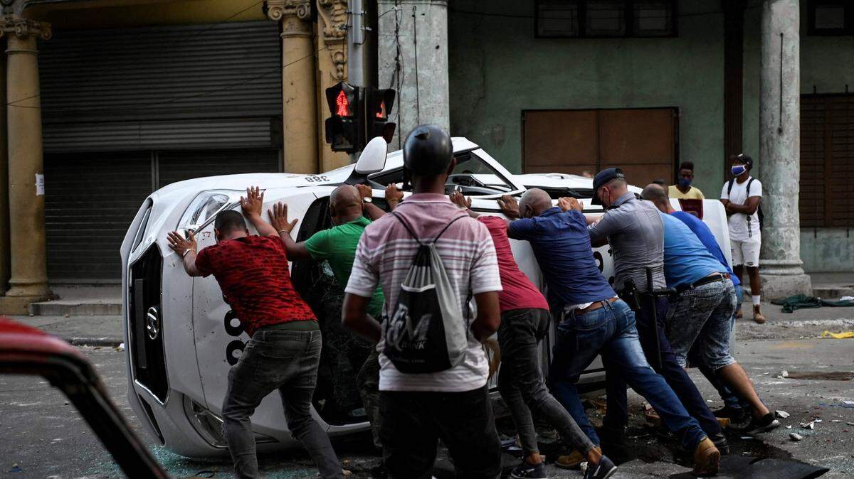 Personas empujan un coche volcado en la calle en el marco de una manifestación contra el presidente cubano, Miguel Díaz-Canel, en La Habana, el 11 de julio de 2021. Miles de cubanos participaron el domingo en inusuales protestas contra el gobierno comunista, marchando por una ciudad al grito de "Abajo la dictadura" y "Queremos libertad".