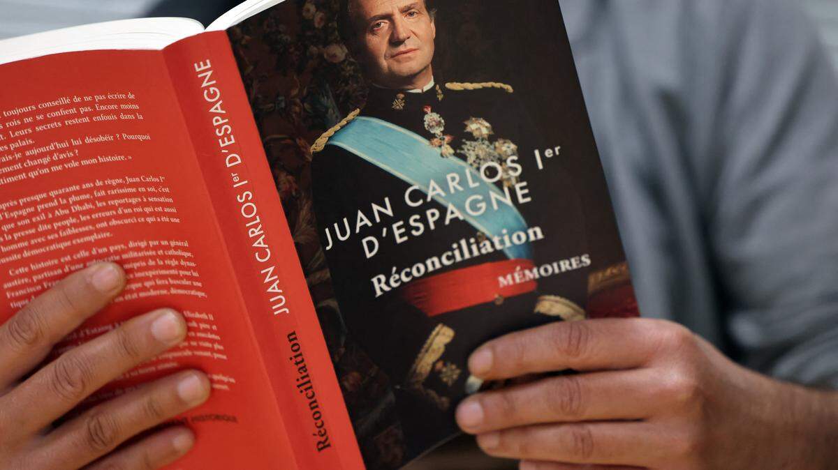 This picture taken in Madrid on November 13, 2025 shows a person holding the book "Juan Carlos 1er d'Espagne. Reconciliation", the French edition of former Spanish King Juan Carlos's memoirs. The release of exited former Spanish King Juan Carlos's memoirs has sparked renewed debate in Spain over his legacy and ties to the late dictator General Francisco Franco. Its publication coincides with the 50th anniversary of Franco's death on 20 November 1975 and the commemoration of Juan Carlos's proclamation as king two days later. In the book, the 87-year-old former monarch reflects on his role in Spain's transition to democracy, his strained family relationships, and the "mistake" of accepting millions of euros from Saudi Arabia. (Photo by Thomas COEX / AFP) (Photo by THOMAS COEX/AFP via Getty Images)