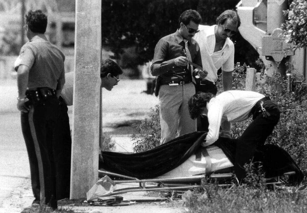 El cadáver de Carl Brown es subido a una camilla, junto a un poste contra el que fue aplastado tras recibir un disparo de un amigo de las víctimas dentro del cercano taller de soldadura y maquinaria Bob Moore en North River Road.
