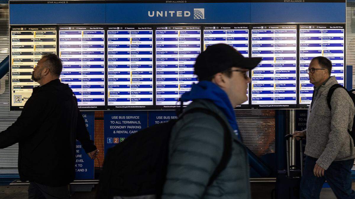 CHICAGO, ILLINOIS - NOVEMBER 30: Travelers move past a United Airlines flight board on a pedestrian bridge in Terminal 1 at O'Hare International airport on November 30, 2025 in Chicago, Illinois. The Federal Aviation Administration is gearing up for the busy Thanksgiving travel time and is ready to get more than 360,000 flights to their destinations. (Photo by Jim Vondruska/Getty Images)