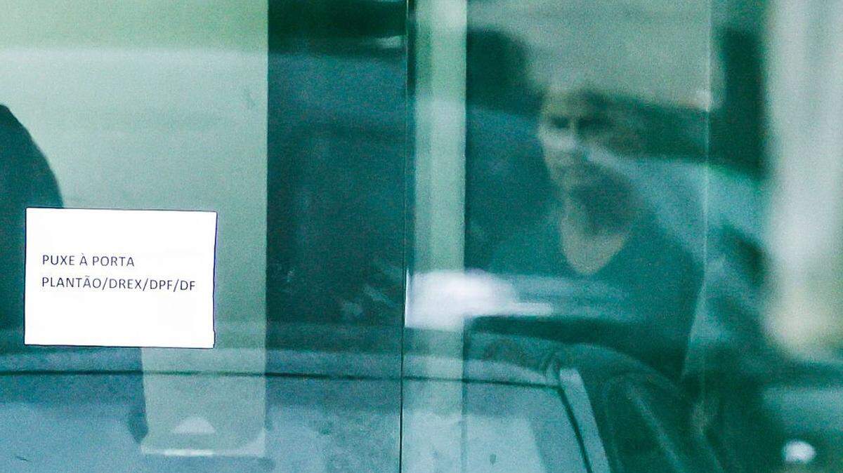 Brazil's former President (20192023) Jair Bolsonaro is seen through the door of the Federal Police headquarters, where he is imprisoned, at the end of former First Lady Michelle Bolsonaro's (out of frame) visit in Brasilia, Brazil on November 23, 2025. Bolsonaro, sentenced last September to 27 years in prison for a failed coup attempt but not yet serving his term, was taken into police custody on November 22 after trying to burn the ankle monitor tracking his house arrest, though he later claimed he acted out of "paranoia" when attempting to disable the device. (Photo by Sergio Lima / AFP via Getty Images)