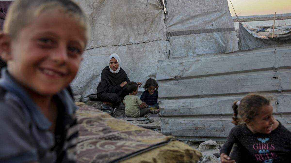 Niños se sientan junto a una tienda de campaña en un campamento improvisado a lo largo de la calle Al-Rasheed, en el oeste de la Ciudad de Gaza, el 7 de octubre de 2025.