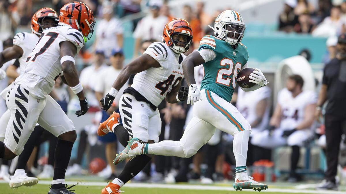 El running back de los Dolphins, De’Von Achane (der.), corre con el balón ante la marca del safety de los Bengals de Cincinnati, Jordan Battle (27), en la primera mitad del partido de la NFL celebrado el 21 de diciembre de 2025 en el Hard Rock Stadium en Miami Gardens, Florida.