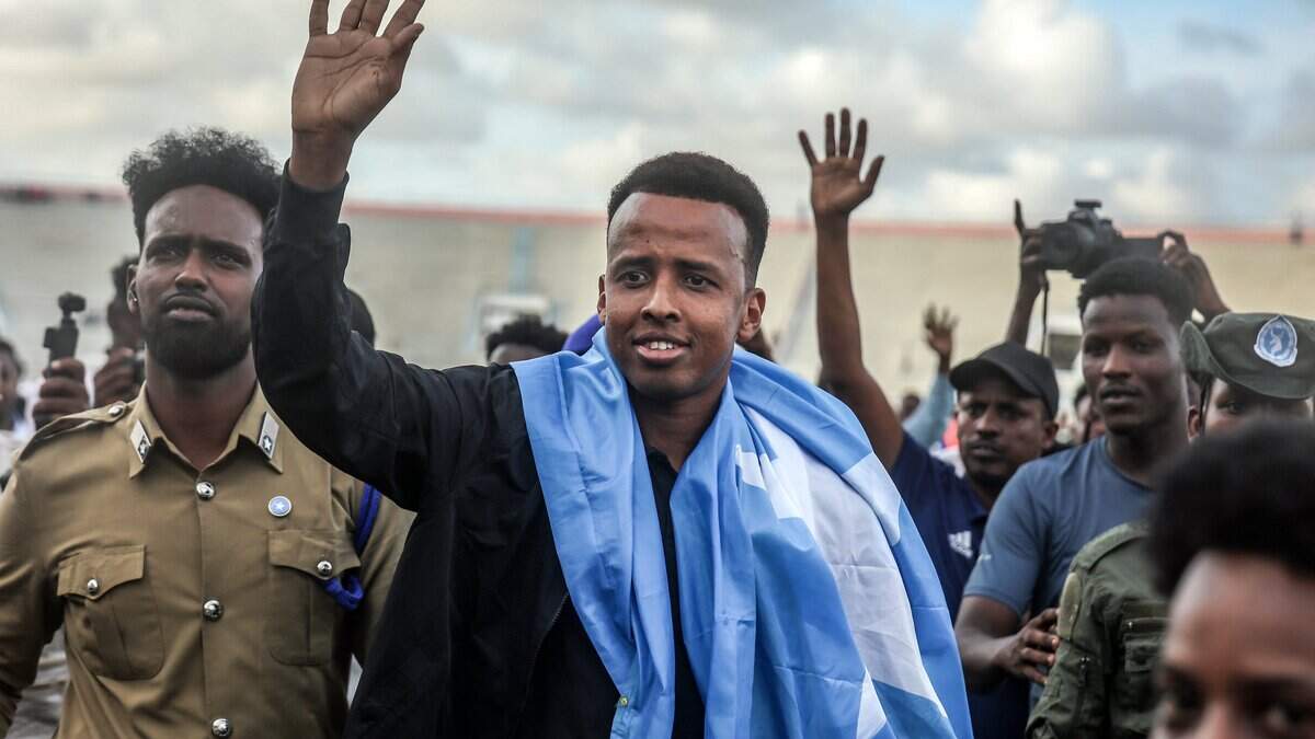 TOPSHOT - Somali international referee Omar Abdulkadir Artan waves to supporters while draped in the Somali flag as he is welcomed ahead of a solidarity football match after returning to Somalia in Mogadishu on June 10, 2026. Somali referee Omar Artan, who was denied entry to the United States for the World Cup, returned to a hero's welcome in Mogadishu and vowed to take part in the next tournament in 2030. Artan's rejection has sparked outrage at home.Artan, who in 2025 was named men's referee of the year by the Confederation of African Football (CAF), was barred from entering the US on Saturday after arriving at Miami International Airport. (Photo by Hassan Ali Elmi / AFP via Getty Images)