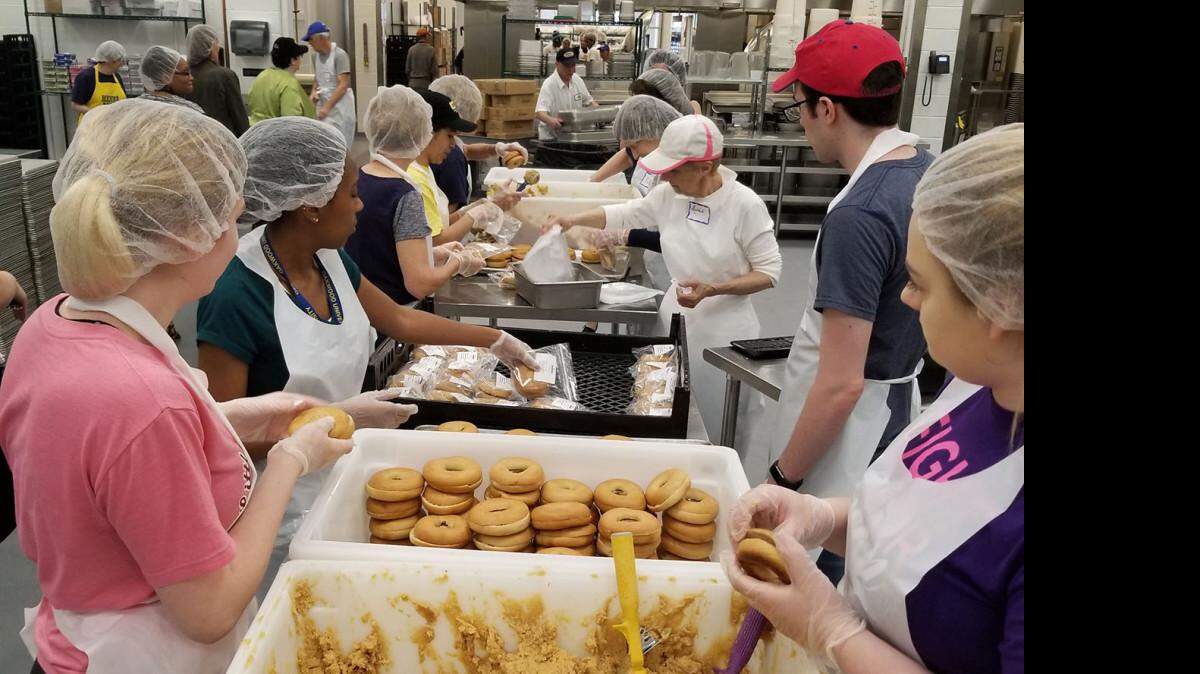 Voluntarios de MANNA preparan sándwiches con bagels integrales y hummus.